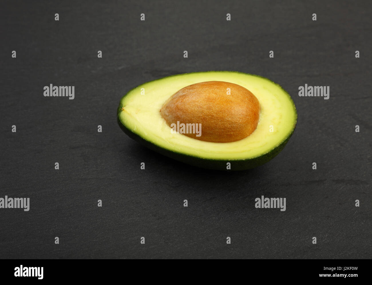 L'un vert frais mûrs avec la moitié d'avocat Pierre pit sur fond d'ardoise noire, détail, Close up, high angle view Banque D'Images