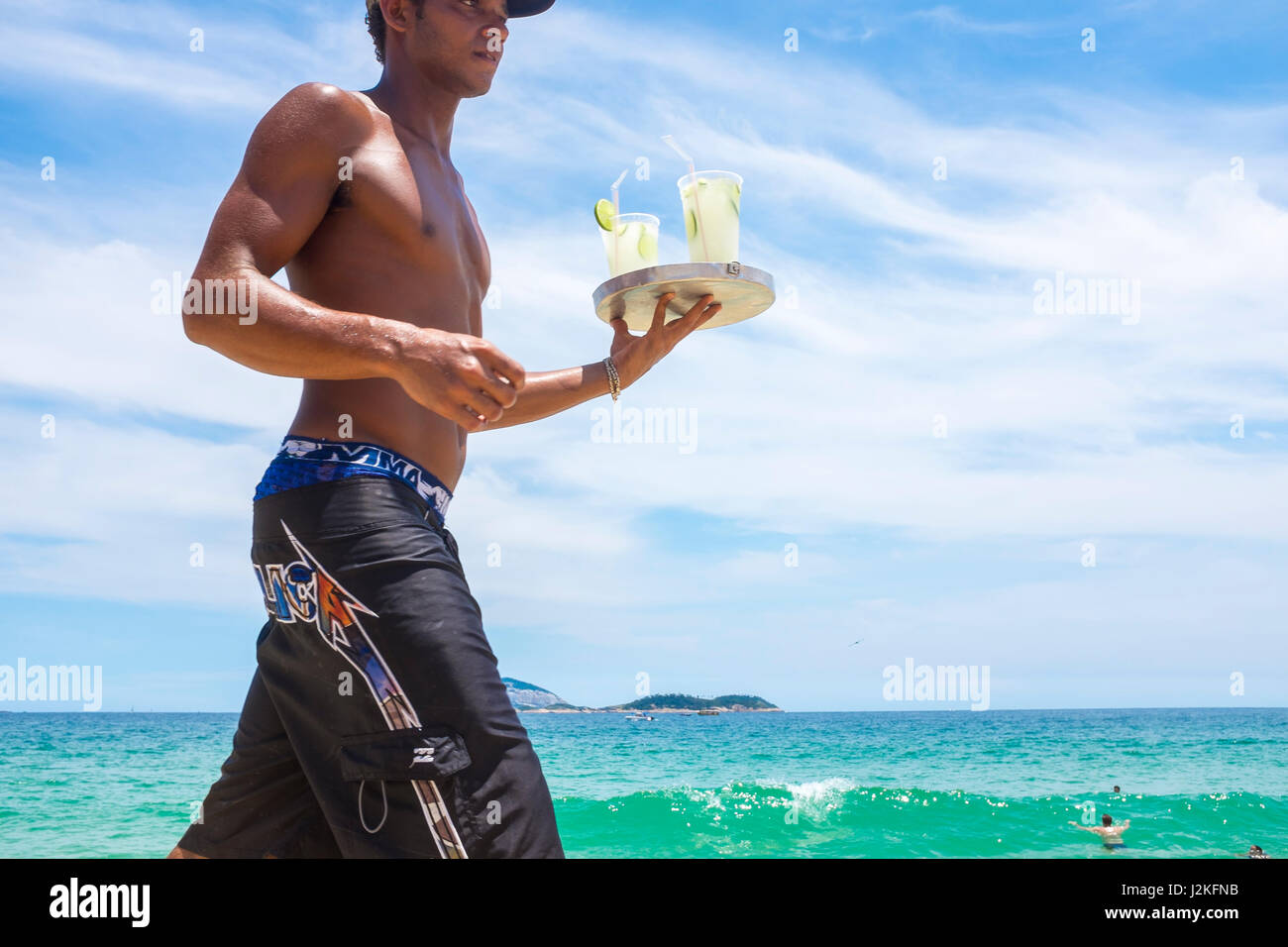 RIO DE JANEIRO - le 22 janvier 2017 : jeune Brésilien vendeur porte un plateau de caipirinha cocktails dans le soleil de midi sur la plage d'Ipanema. Banque D'Images