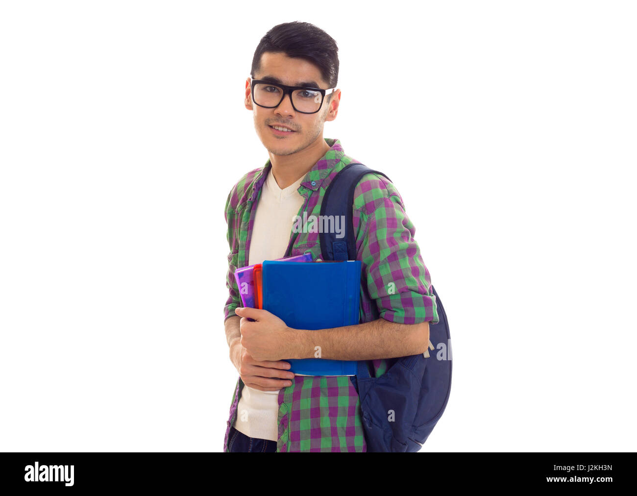 Jeune homme souriant avec des cheveux noirs en blanc T-shirt et chemise à carreaux avec sac à dos bleu holding books sur fond blanc en studio Banque D'Images