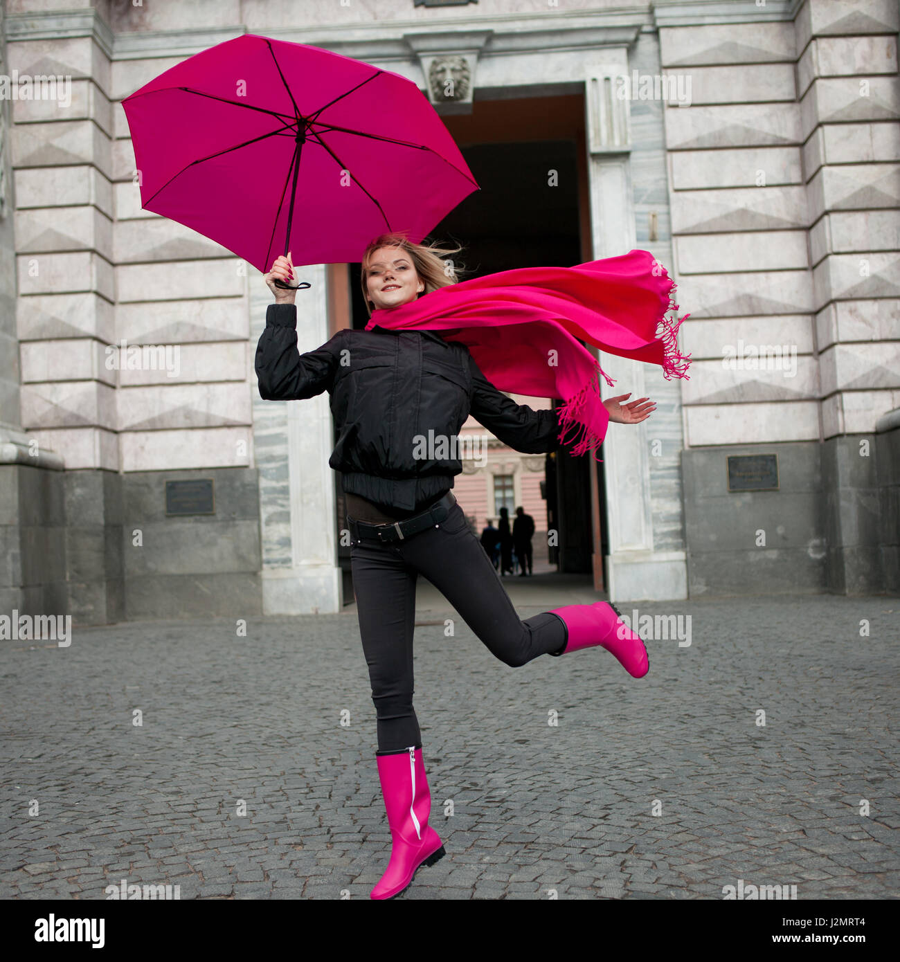 Très belle jeune femme blonde et heureuse avec parapluie colorés sur la  rue. Fille dans une écharpe rose vif, des bottes en caoutchouc et parapluie  marcher dans une ville pluvieuse Photo Stock -