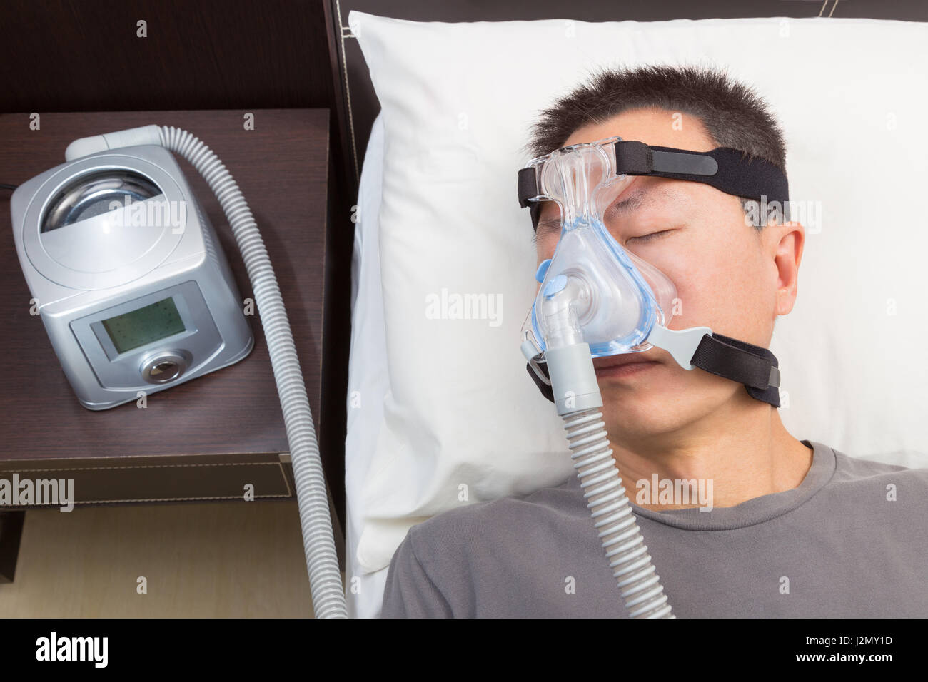 L'homme asiatique avec l'apnée du sommeil à l'aide d'appareil CPAP, le port  de masque harnais connexion au tube d'air, selective focus sur le masque et  le harnais de l'homme Photo Stock -
