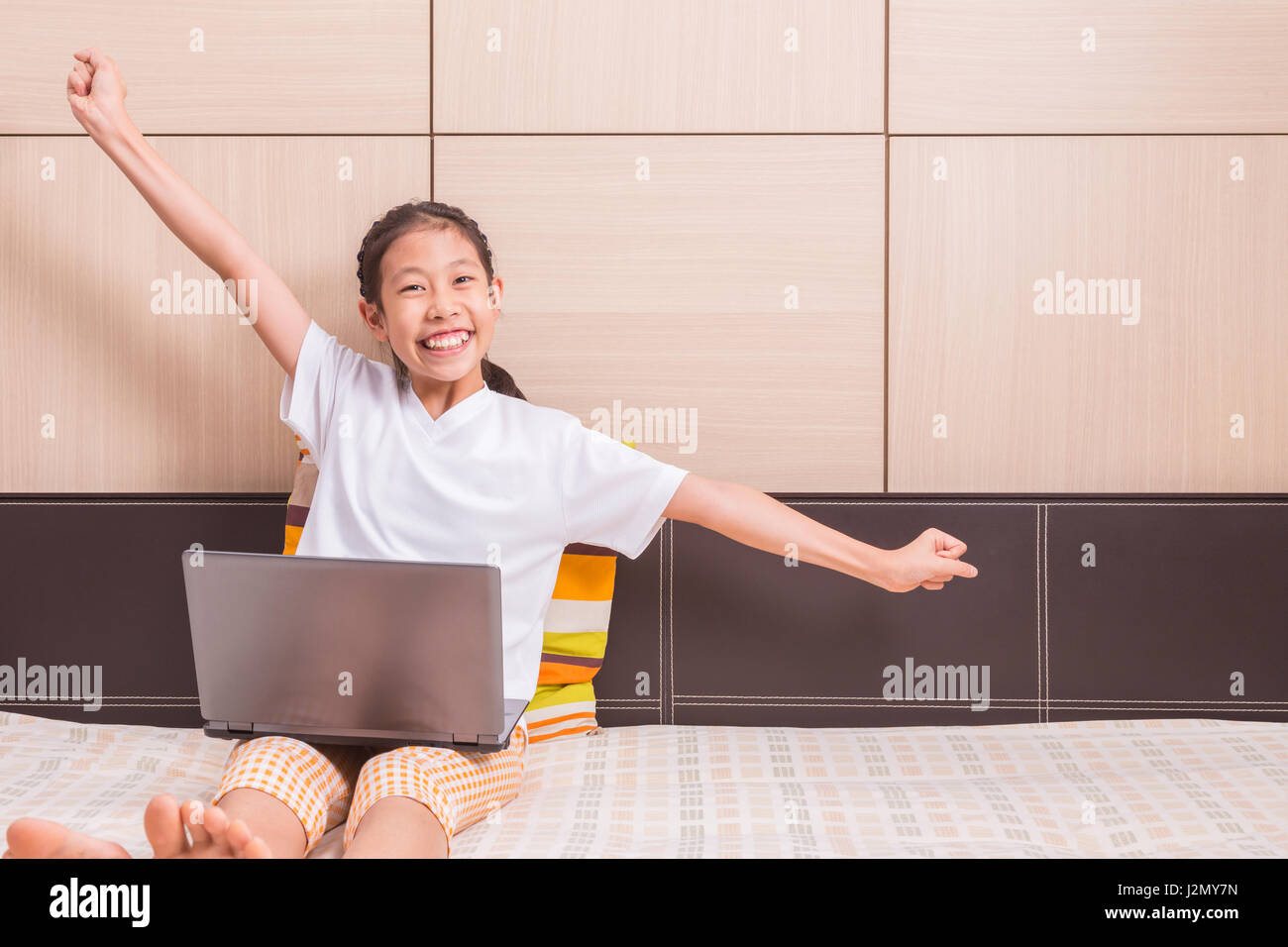 Happy smiling asian girl et excité à l'aide d'ordinateur portable à l'étude sur son lit, ses bras dans un état excité et réussie, de la place pour poser copie Banque D'Images