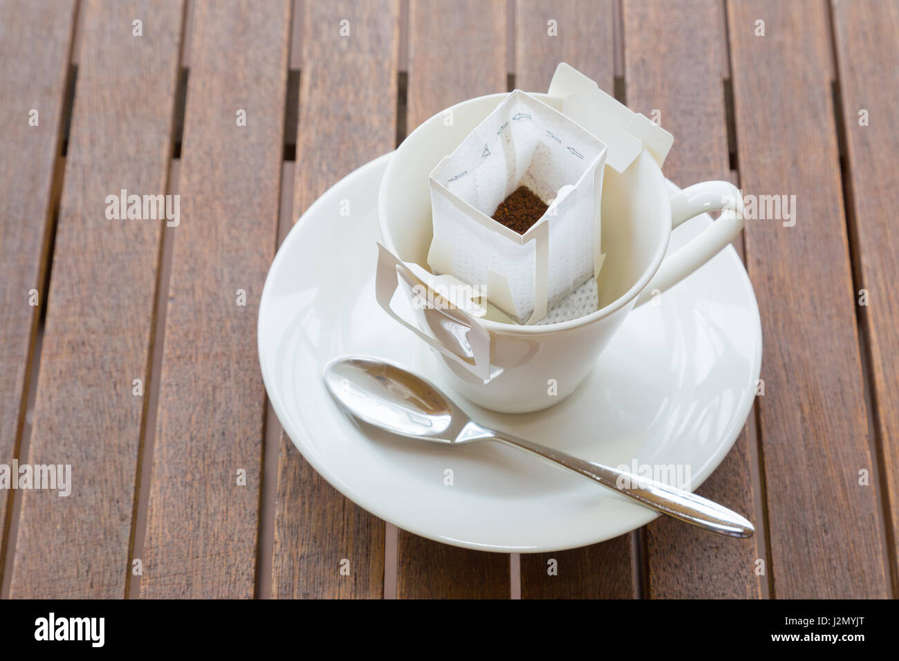 Tasse à café blanc et la cuillère avec du blanc mélangé pré-emballés dans du café filtre papier mis sur table boisée Banque D'Images