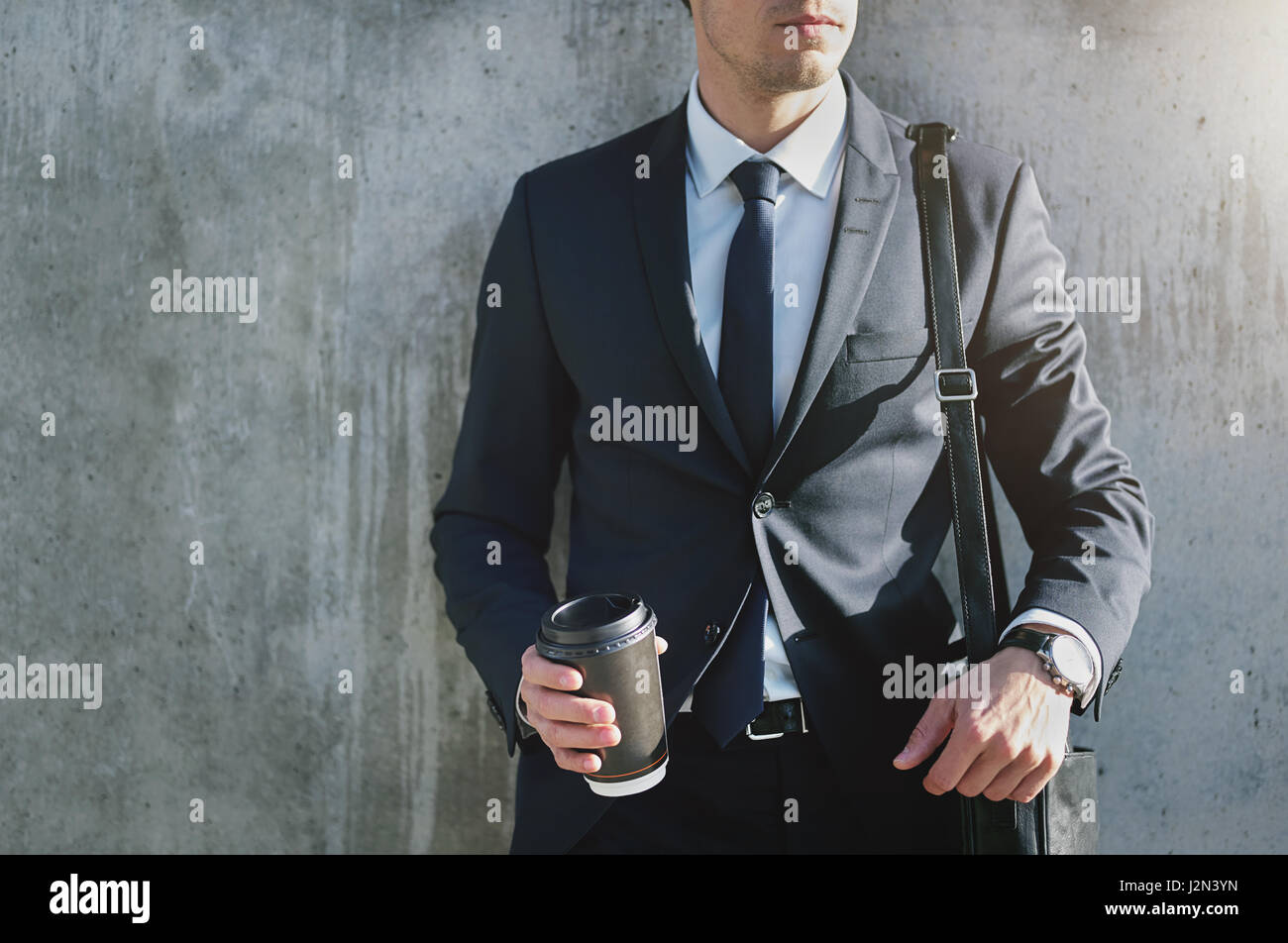 Un homme portant costume élégant avec la tasse de café debout près du mur gris. Banque D'Images