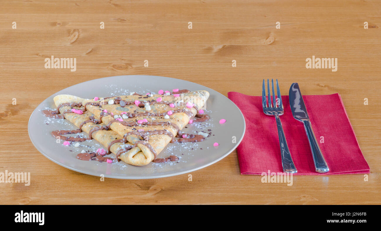 La crêpe avec du chocolat et crème de chocolat et pure servi sur assiette blanche sur une table en bois avec fourchette et couteau sur une serviette rouge Banque D'Images