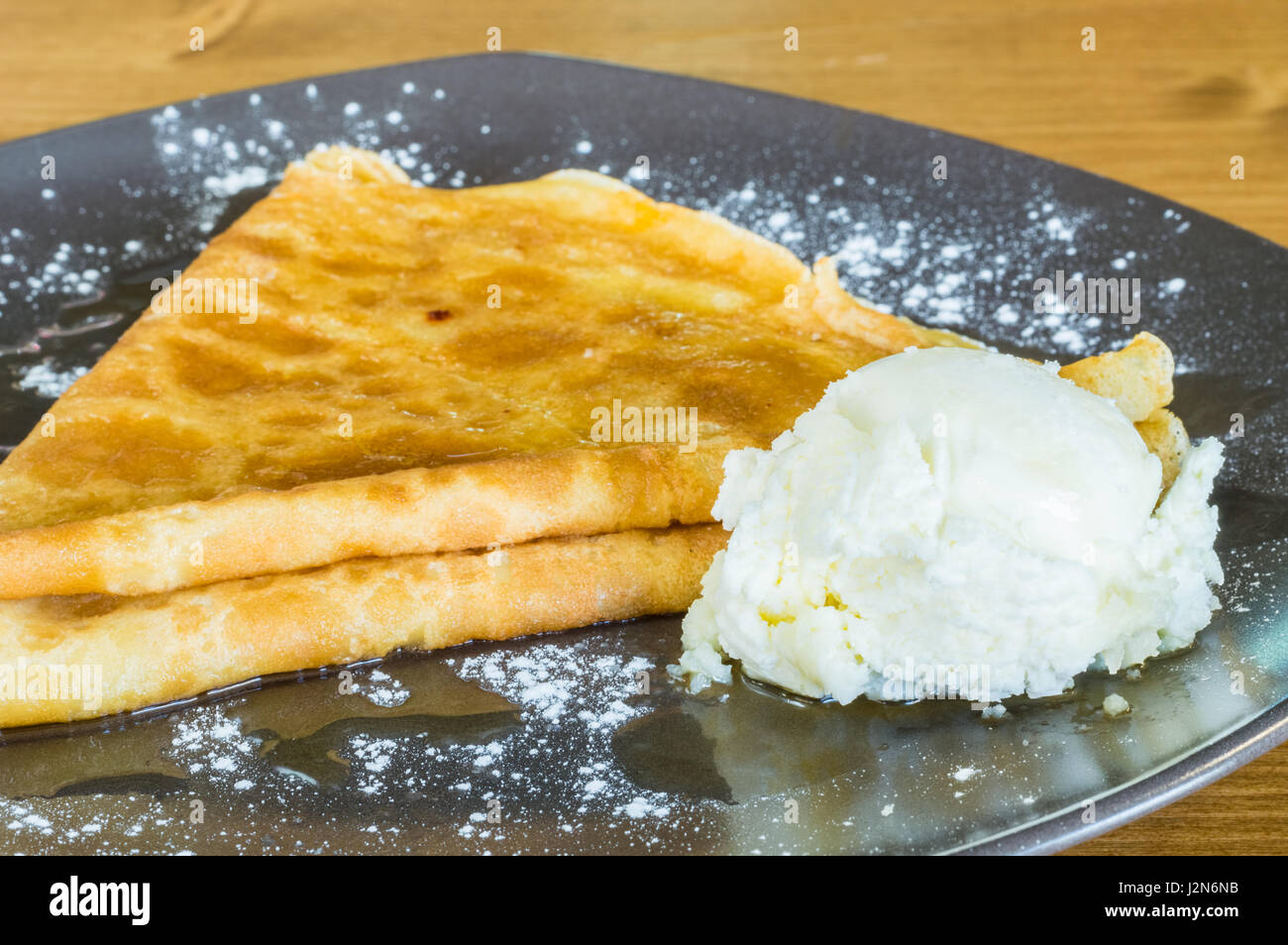Gros plan du crêpe délicieuse avec du miel et de la crème glacée servie sur une plaque gris sur une table en bois Banque D'Images