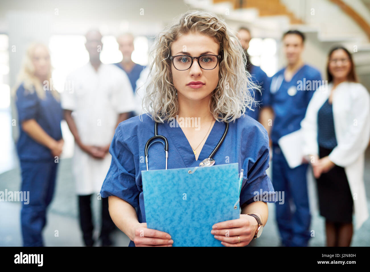 Young female doctor standing in clinique et à la recherche à l'appareil photo. Comité permanent de l'équipe de l'hôpital en arrière-plan Banque D'Images