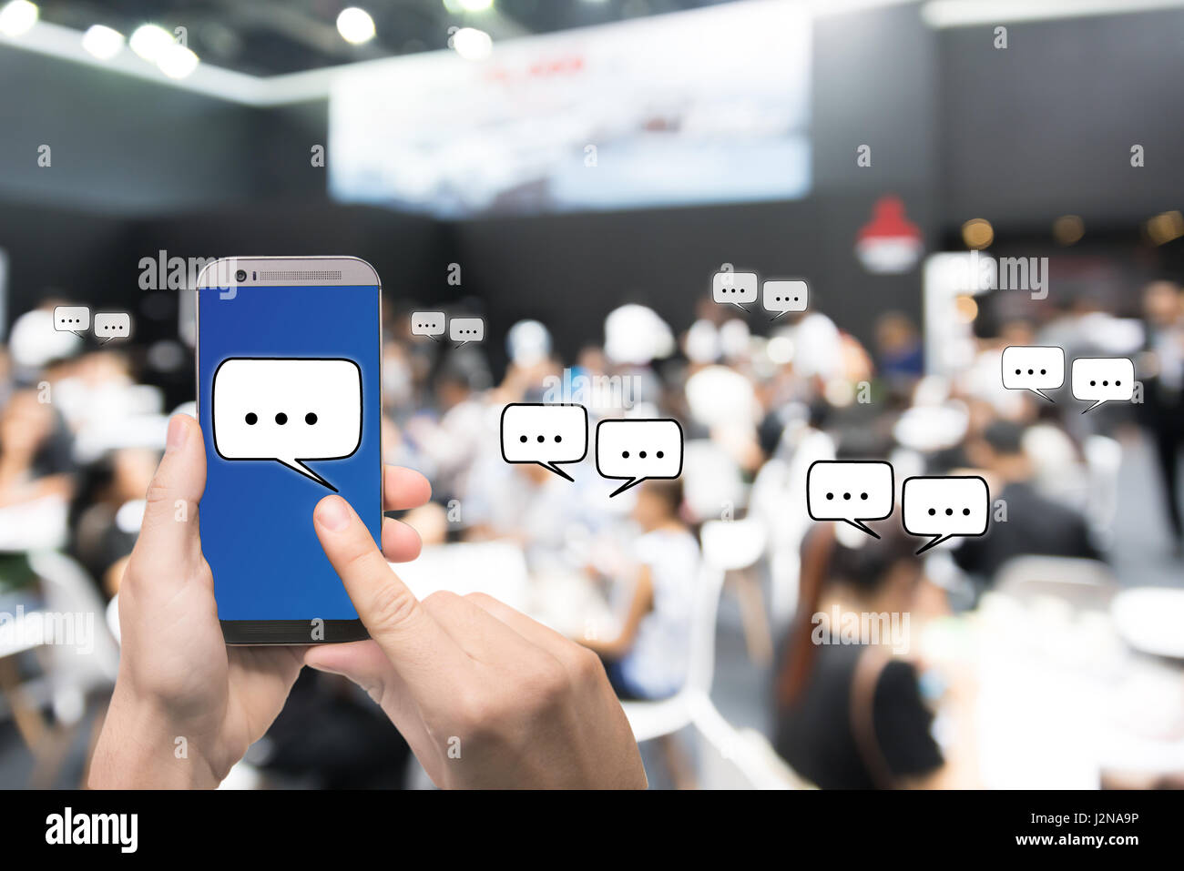 Hand holding mobile phone montrant messages chat en direct sur le réseau social en plus floue Résumé photo de salle de conférence ou salle de séminaire avec assister à Banque D'Images