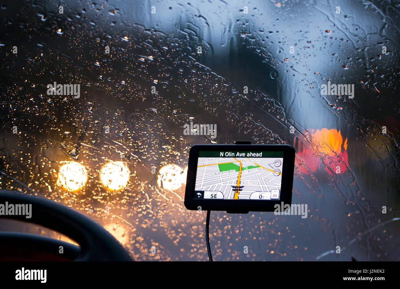 GPS Navigator avec une carte de la ville avec des rues et des routes dans  l'écran d'affichage en mode nuit sur la vitre avec gouttes de pluie et  volant Photo Stock -