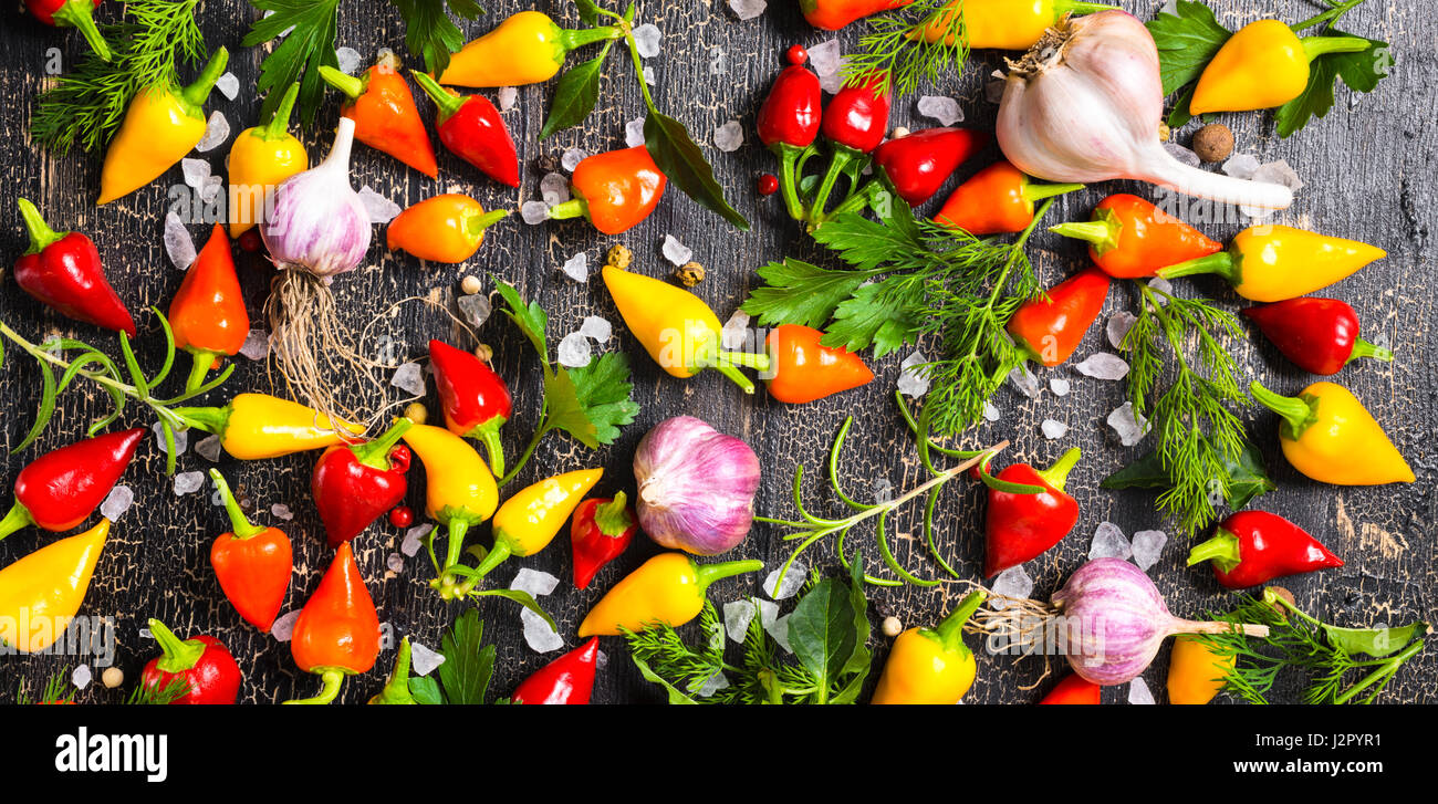 Vue de dessus de jaune à maturité, Red Hot Chili Peppers, sel de mer, verdure différents, les poivrons et l'ail noir sur fond noir des fissures, panorama Banque D'Images