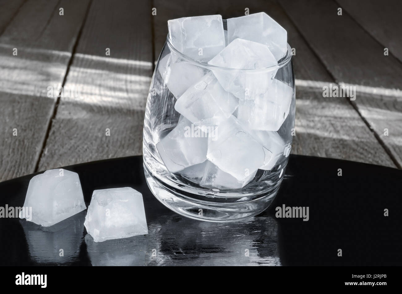 Des cubes de glace dans un verre, fond en bois gris Banque D'Images