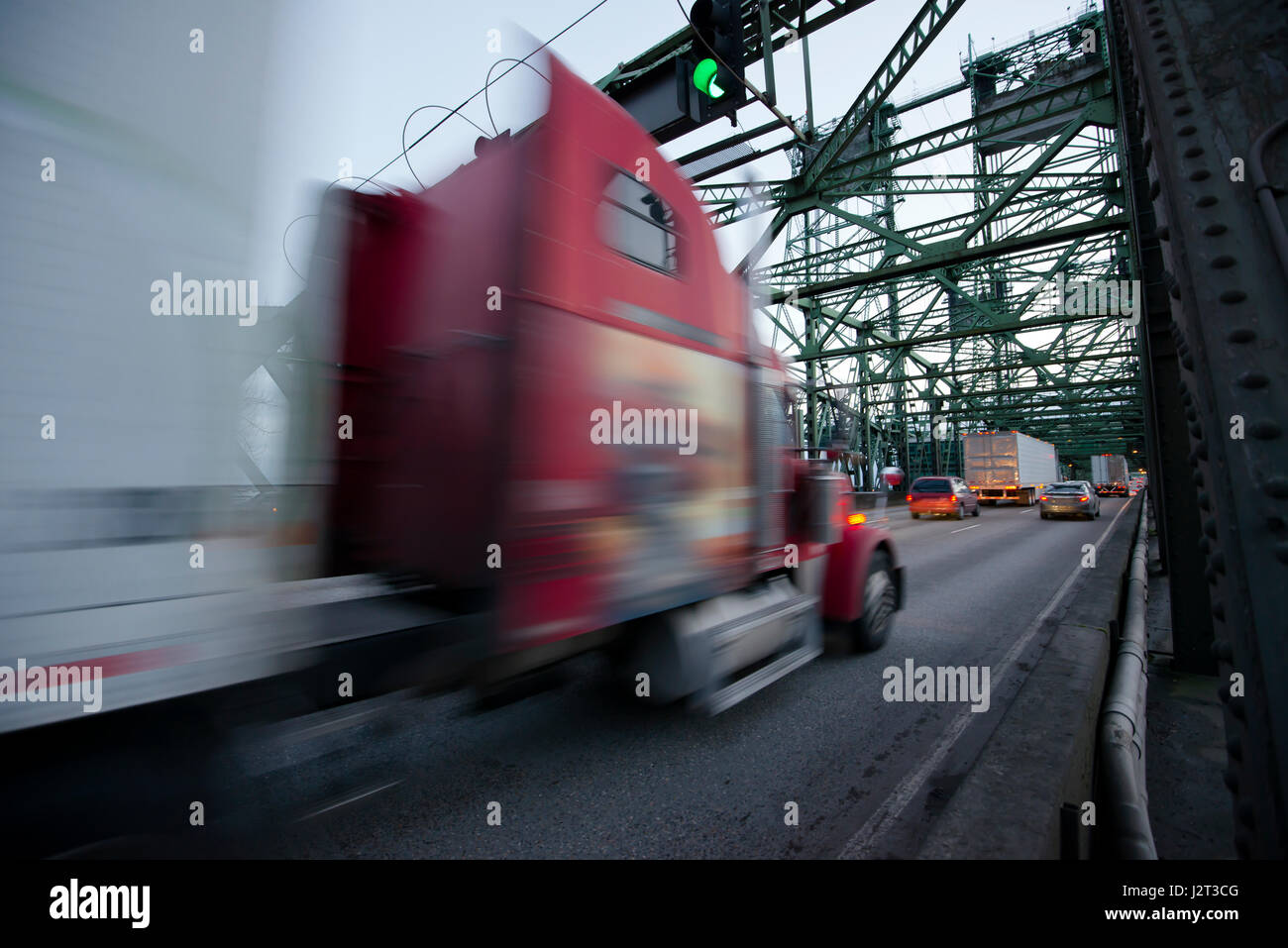 Semi-classique rouge floue avec une remorque de camion sur l'autoroute qui longe le pont en treillis vert sur le feu vert sur l'arrière-plan Banque D'Images