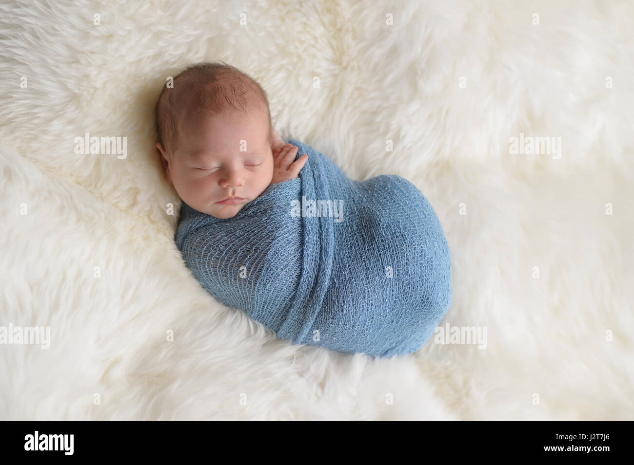 Dormir, neuf jours vieux garçon nouveau-né emmailloté dans un emballage bleu clair. Tourné en studio sur un tapis en peau de mouton blanc. Banque D'Images