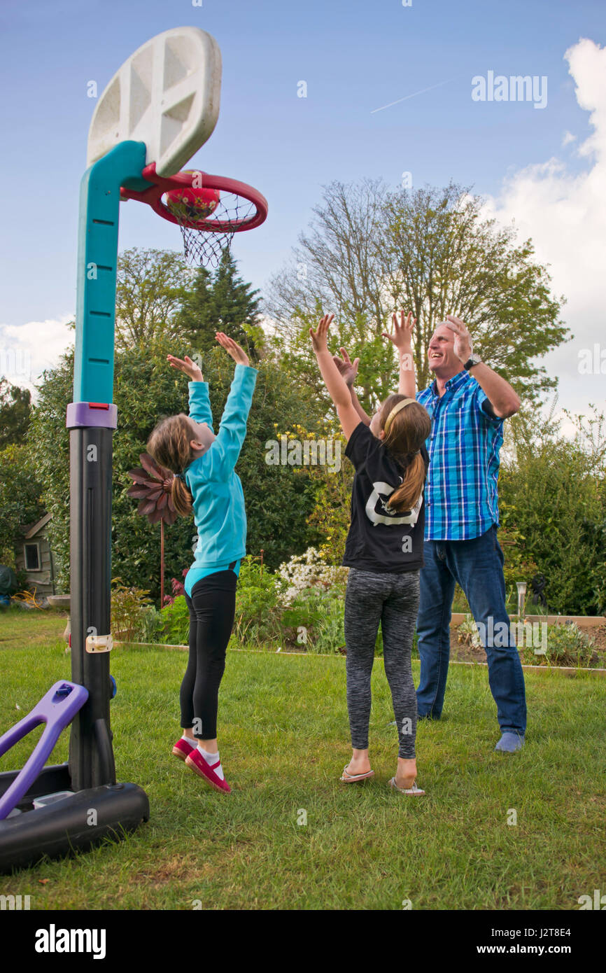 Vue verticale d'un grand-père jouant au basket-ball avec ses petits-enfants dans le jardin. Banque D'Images