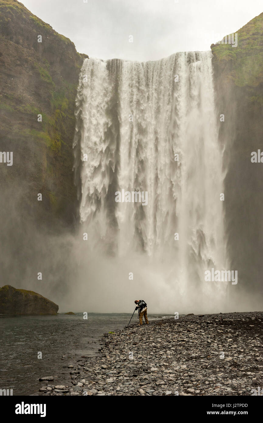 Photographe mâle au bas de cascade de Skogafoss, de photographier, de brume, de cascades d'Islande. Banque D'Images