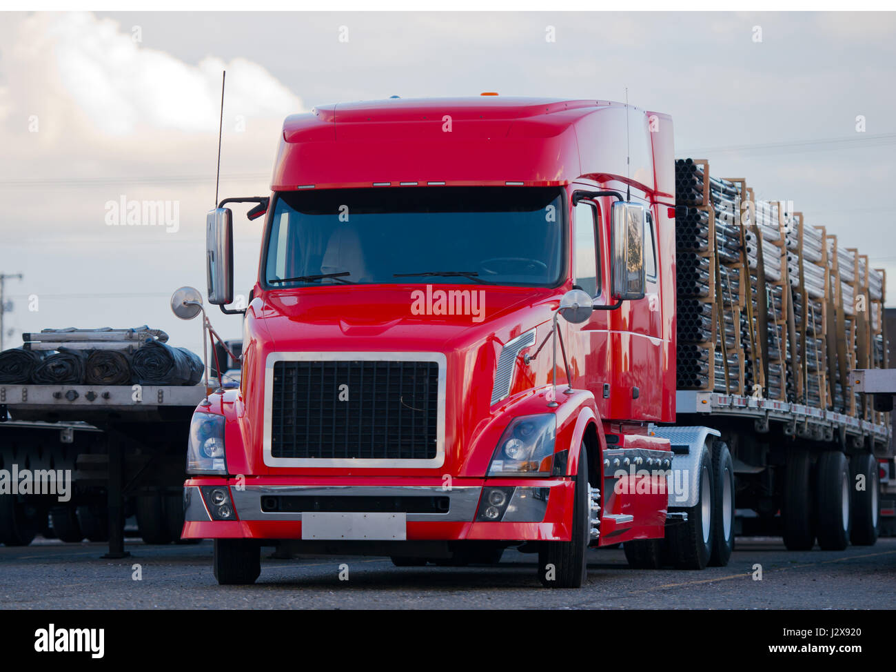 Rouge vif puissant semi truck avec cabine basse d'accessoires modernes en acier inoxydable avec une remorque à fond plat, chargées de tuyaux en plastique Banque D'Images