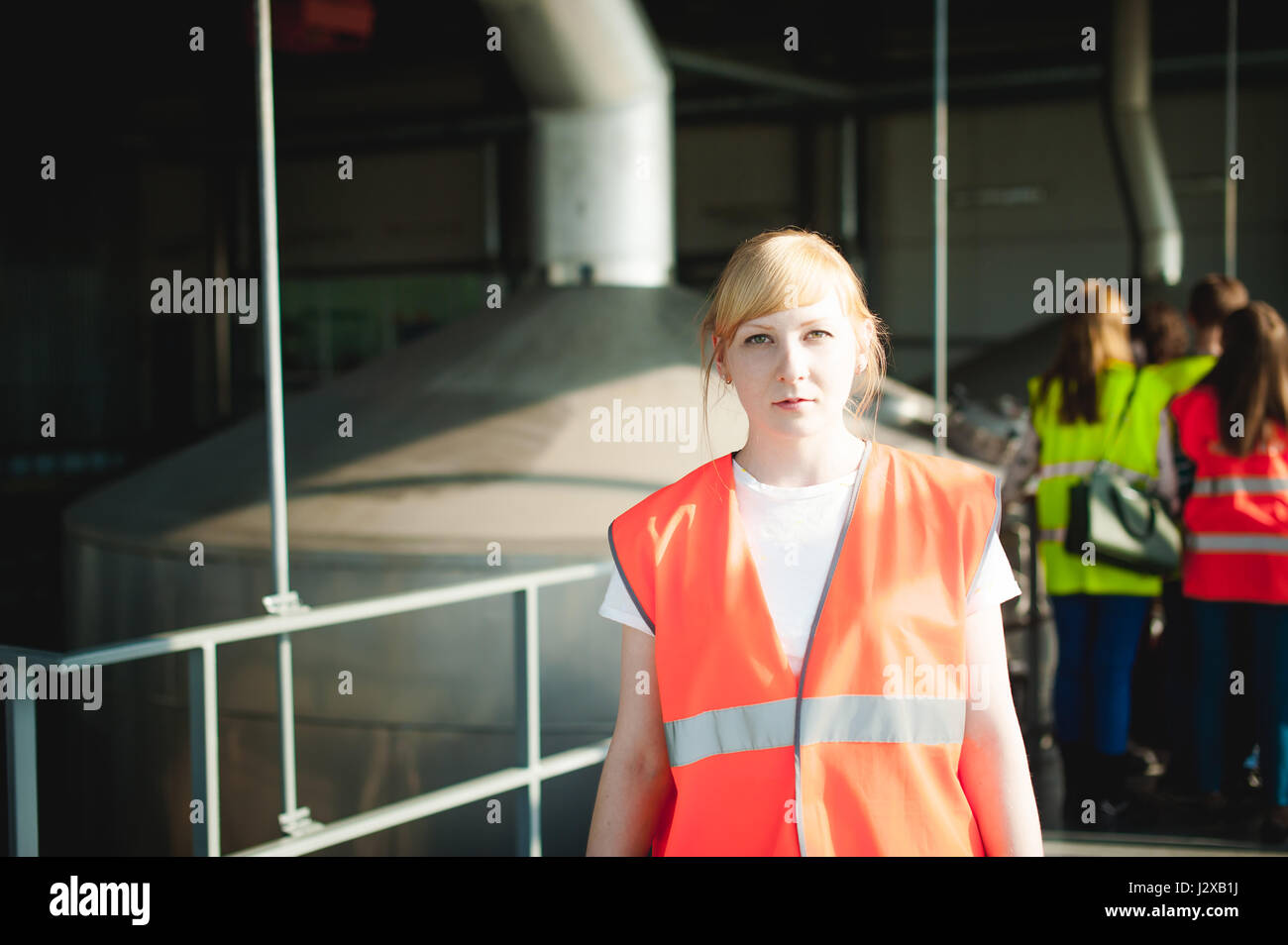 Femme blonde en salopette, sur la visite de la brasserie plante dans les locaux industriels, au milieu d'une foule de gens dans les gilets pare-balles, d'inspecter une usine pour la formation p Banque D'Images