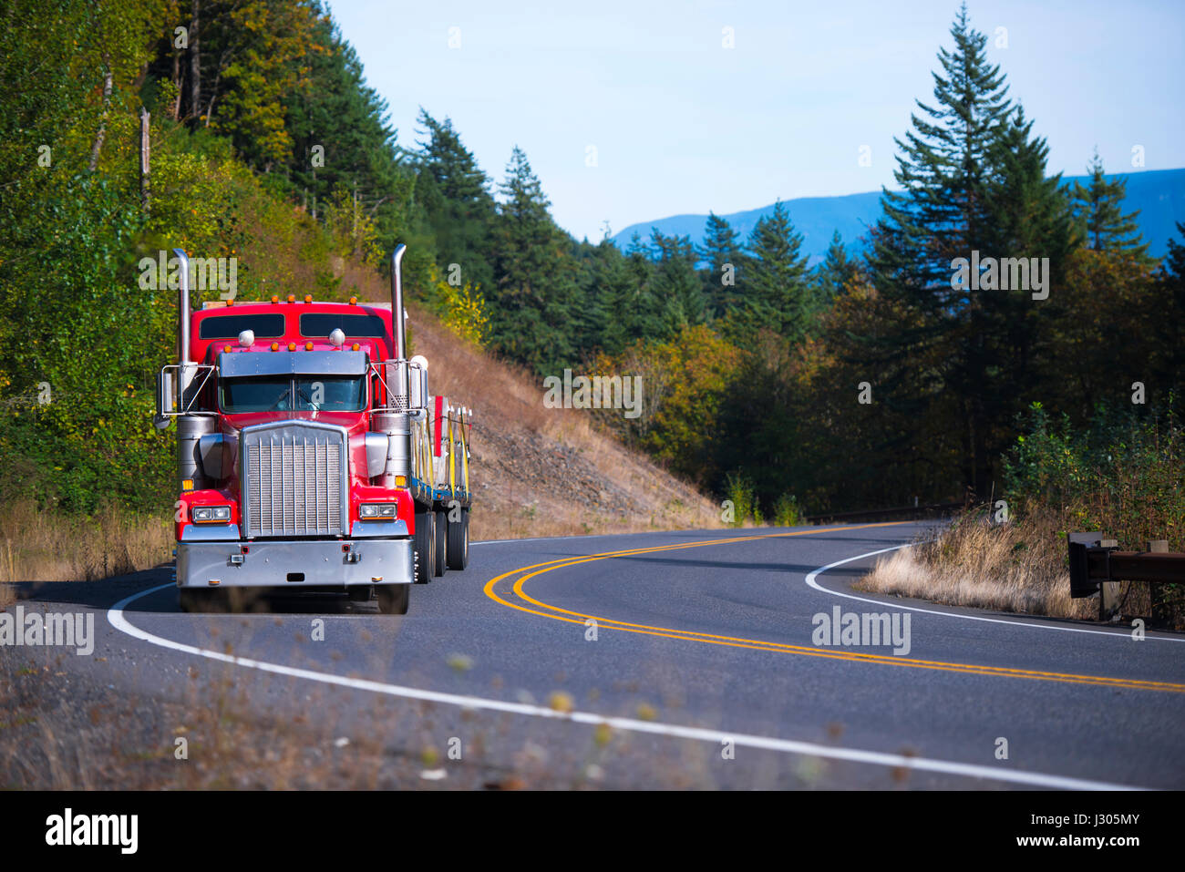 Camion semi-remorque rouge classique avec calandre chromée et tuyaux d'échappement verticaux avec remorque à plateau chargée de palettes de chargement commercial dans un virage Banque D'Images