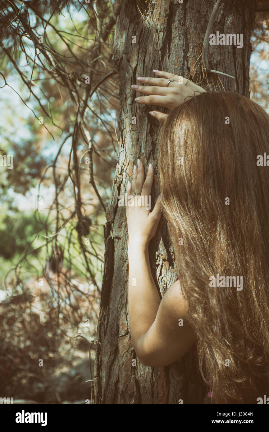 Jeune femme hding peur derrière un arbre Banque D'Images