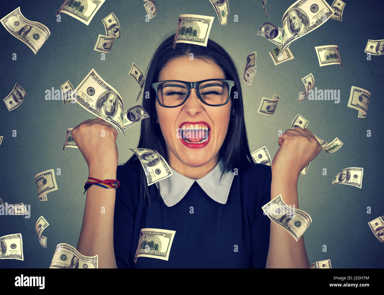 Happy woman Portrait poings pompage exulte de joie célèbre son succès sous la pluie tomber de l'argent dollar bills billets isolé sur mur gris backg Banque D'Images