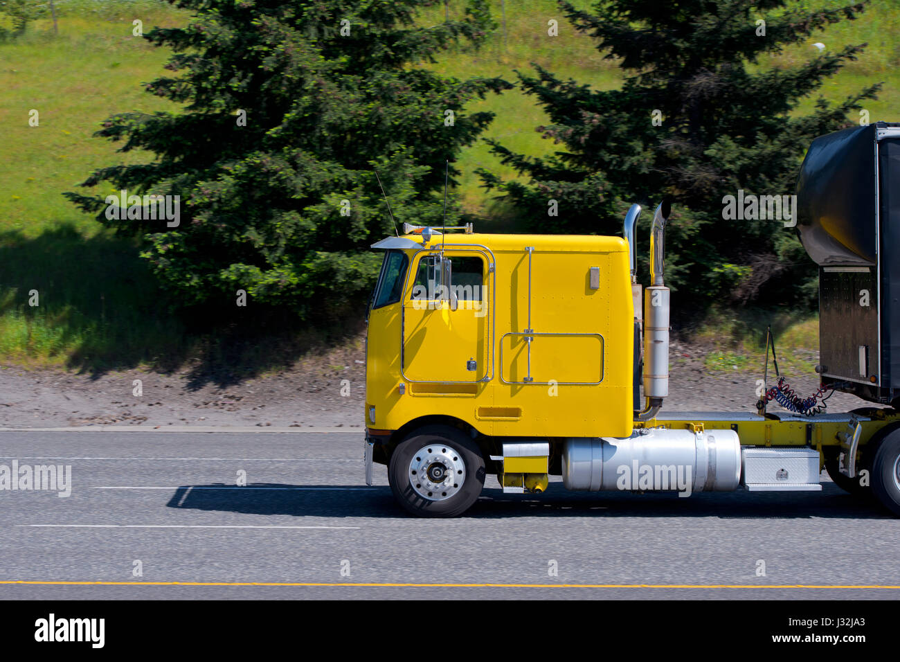 Vieux jaune vif rétro des années précédentes modèle semi-camion sans capot avec une remorque noire continue à transporter des marchandises sur la route avec des arbres Banque D'Images