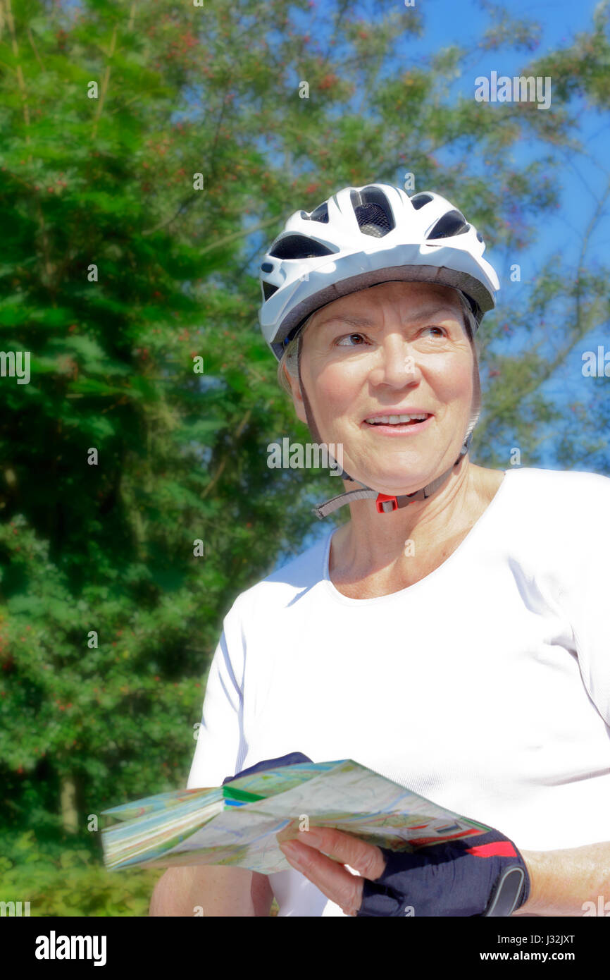 Senior woman à l'extérieur l'été soleil avec casque de vélo, gants, T-shirt blanc et la carte, profiter de la vue, retraite active concept Banque D'Images