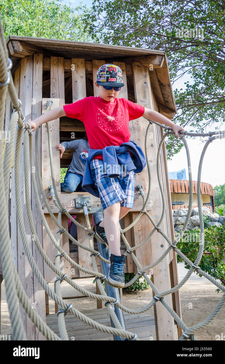 Un jeune garçon traverse un pont de corde qui fait partie d'une escalade dans une aire de jeux pour enfants. Banque D'Images