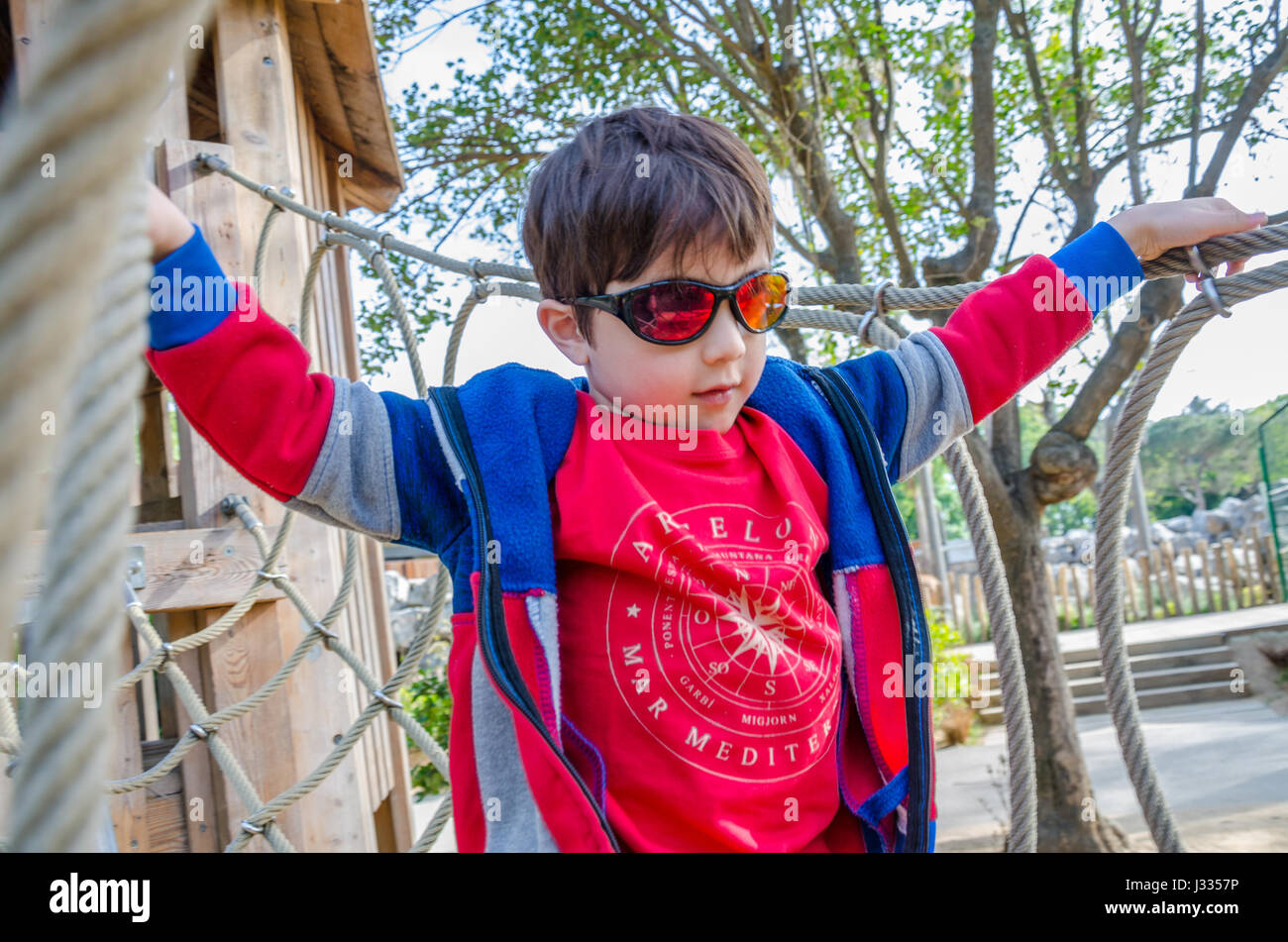 Un jeune garçon traverse un pont de corde qui fait partie d'une escalade dans une aire de jeux pour enfants. Banque D'Images