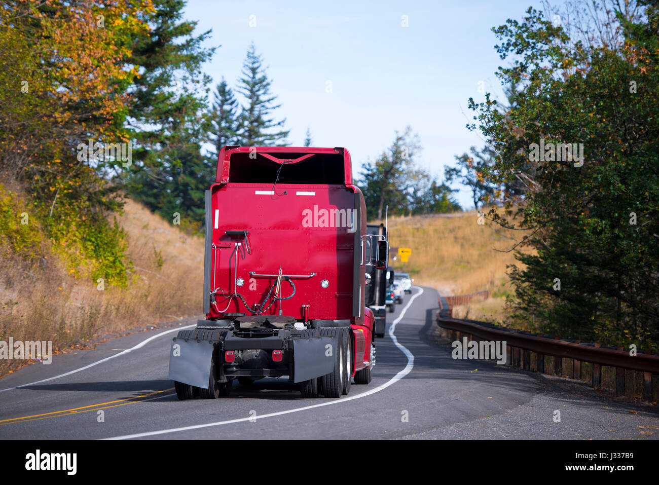Une colonne de plusieurs semi-camions modernes sans remorques avec des becs, et garde-boue, ainsi que les autres voitures se déplacent le long d'une route sinueuse à travers Banque D'Images