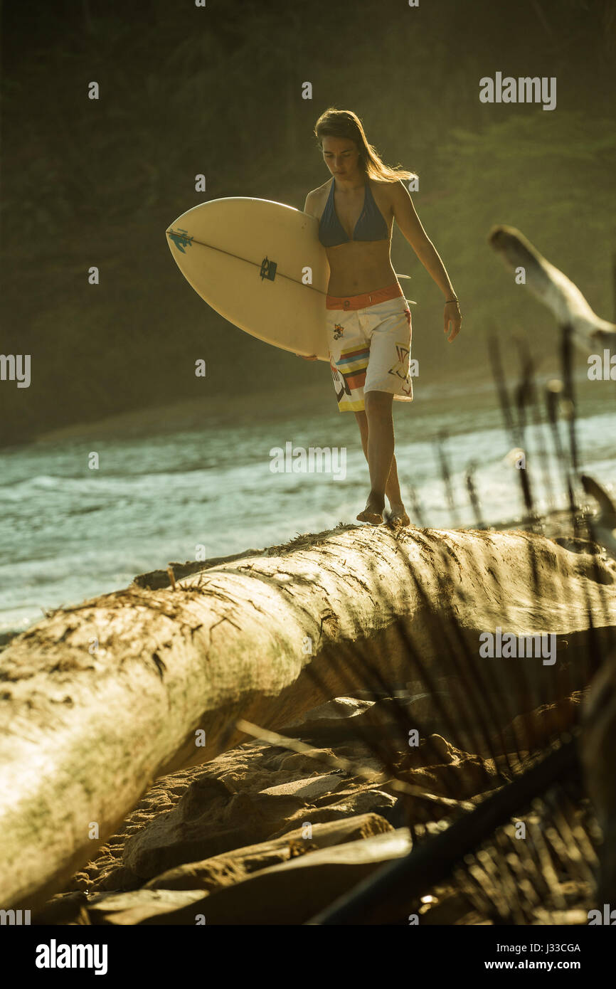 Jeune femme sur un tronc d'équilibrage de surfer sur la plage, à Sao Tomé, Sao Tomé et Principe, Afrique Banque D'Images