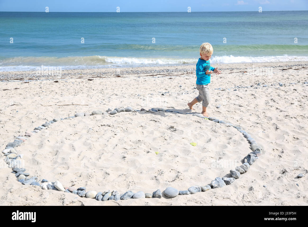 Garçon marchant le long d'un cercle de pierres sur plage, Rytsebaek, Mon île, Danemark Banque D'Images