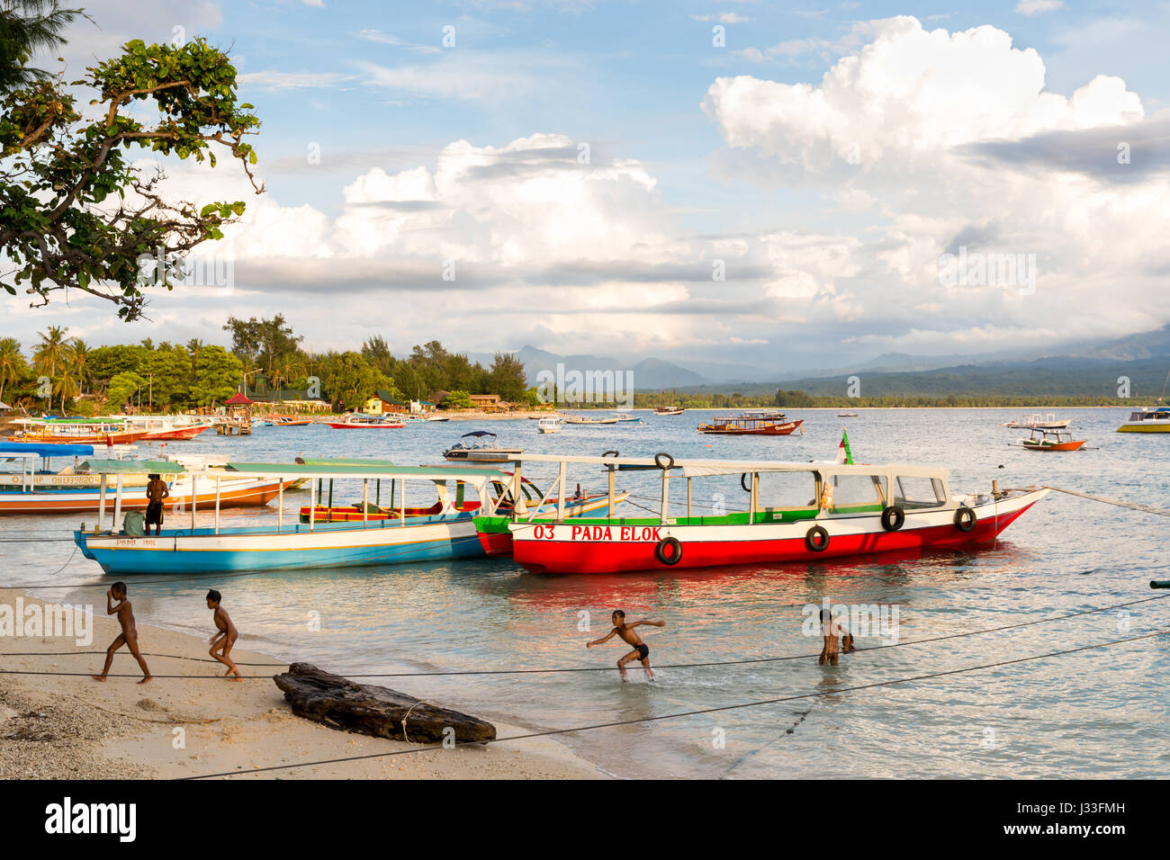 Enfants jouant dans l'eau, bateaux à plage, Gili Air, Lombok, Indonésie Banque D'Images