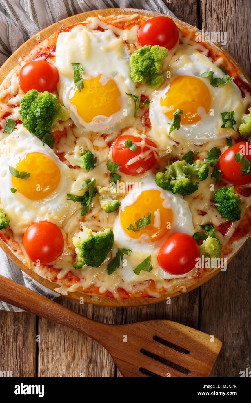 Petit-déjeuner copieux de pizza avec des œufs, le brocoli, les tomates et le persil gros plan sur la table. Vue verticale d'en haut Banque D'Images