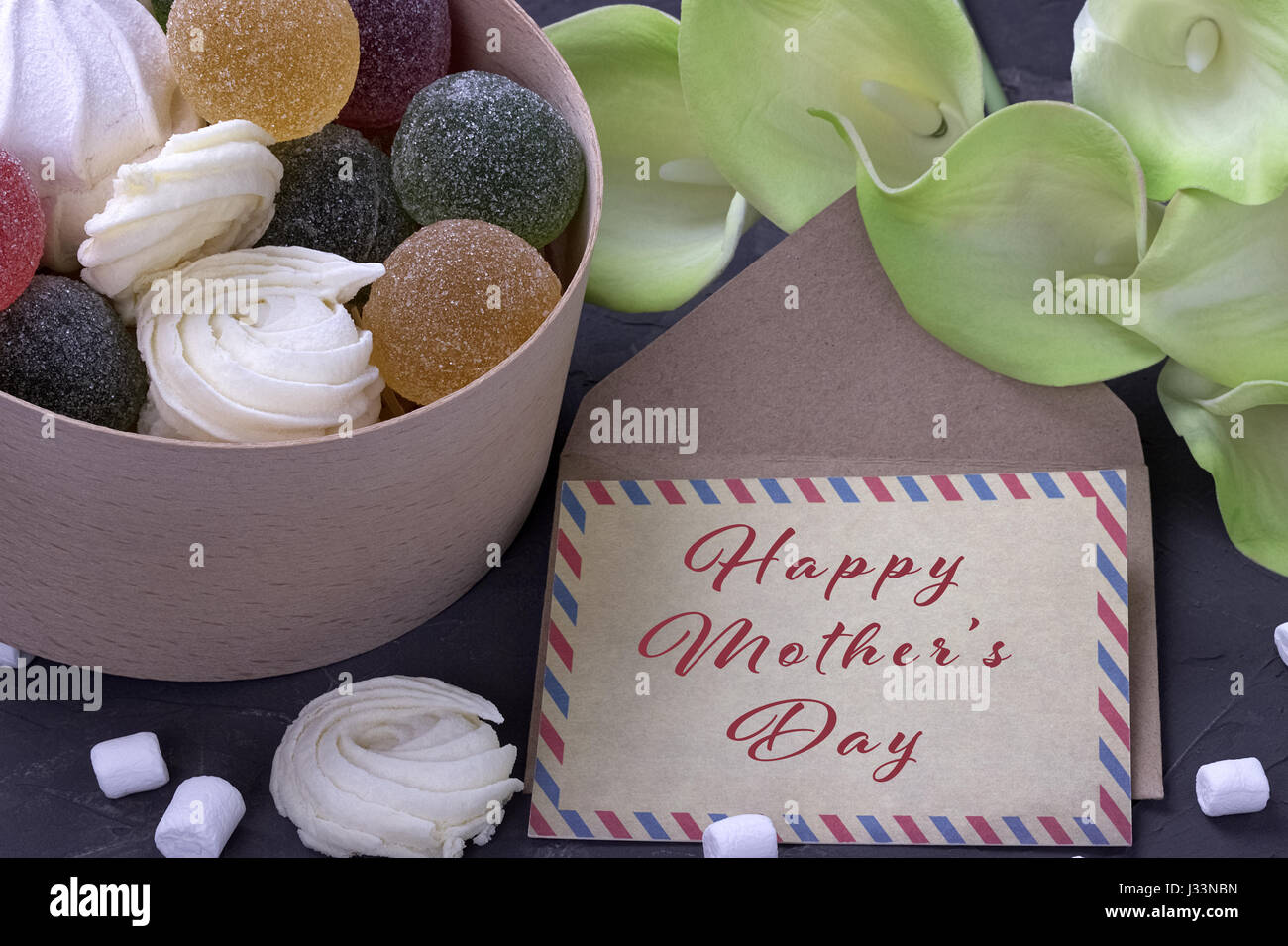 Bouquet de callas jaune vert avec des guimauves marmelade dans une boîte ronde en bois et enveloppe avec lettrage heureux mères le béton gris backg Banque D'Images