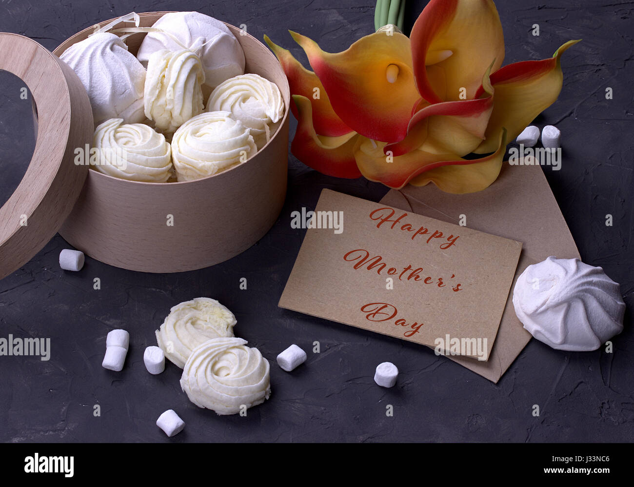 Bouquet de callas jaune rouge avec des guimauves marmelade dans une boîte ronde en bois et enveloppe avec lettrage heureux mères le background de béton gris Banque D'Images