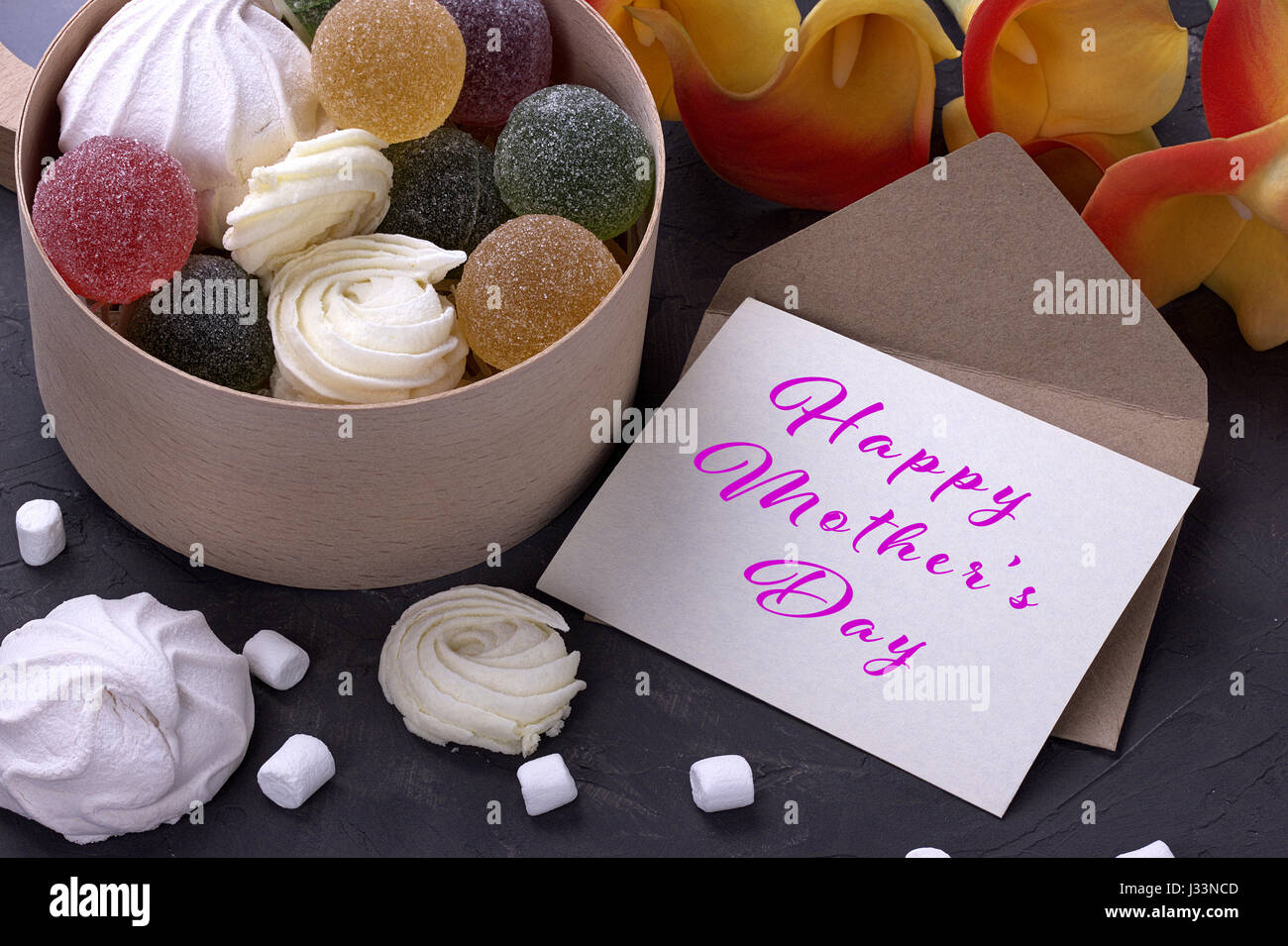 Bouquet de callas jaune rouge avec des guimauves marmelade dans une boîte ronde en bois et enveloppe avec lettrage heureux mères le background de béton gris Banque D'Images