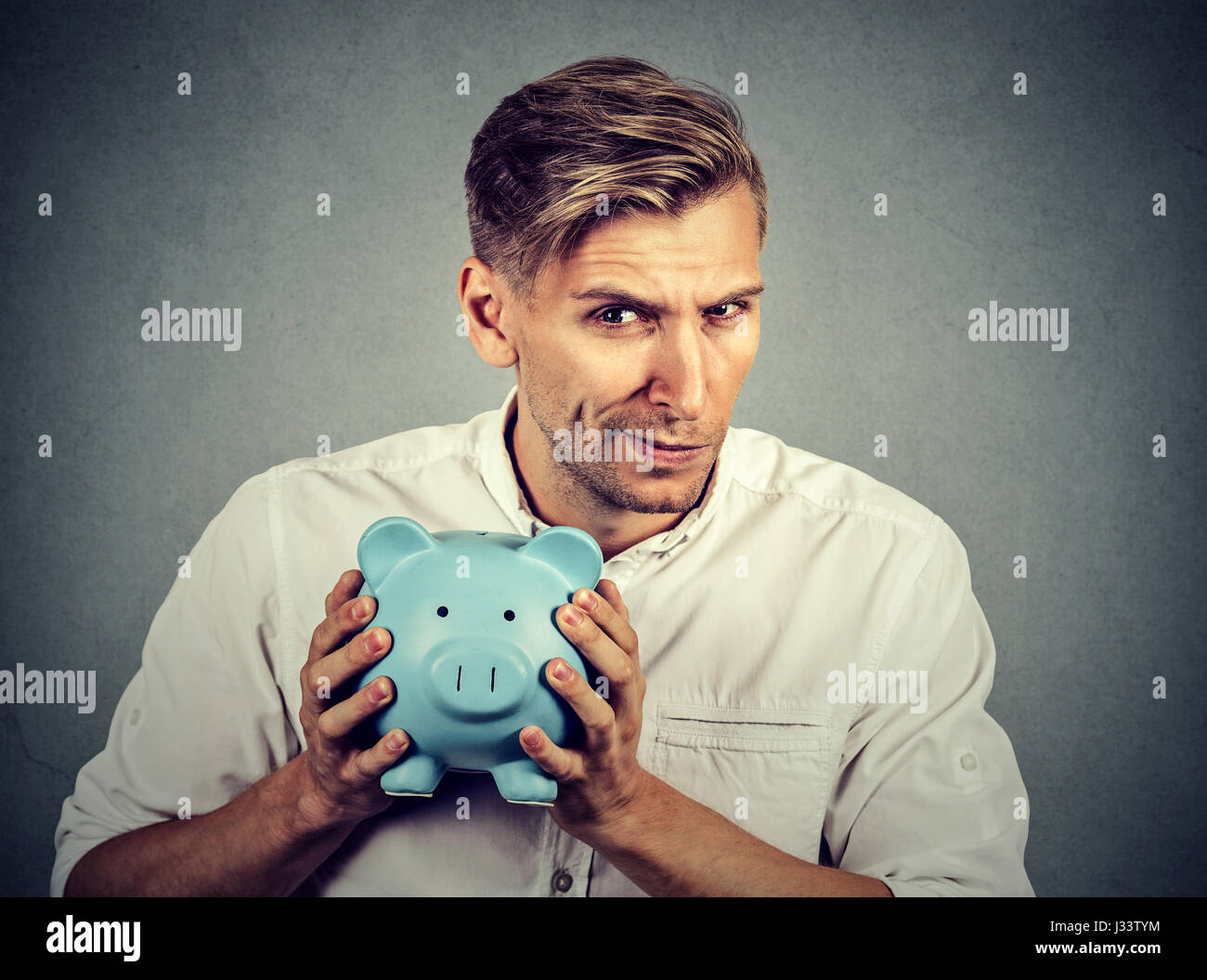 Jeune homme d'affaires avare cupide holding piggy bank isolé sur fond de mur gris Banque D'Images