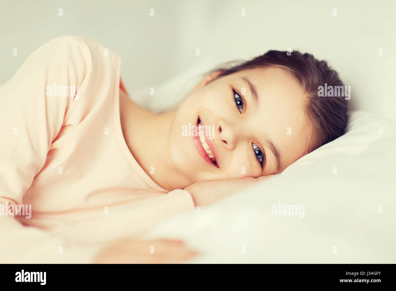 Happy smiling girl lying awake in bed at home Banque D'Images