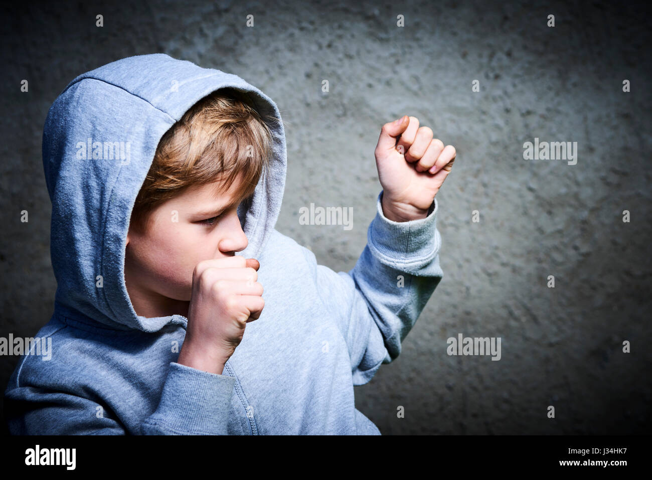Garçon enfant adolescent apparence européenne serra les poings prêt à combattre sur gris grunge wall background, souffler, la protection Banque D'Images