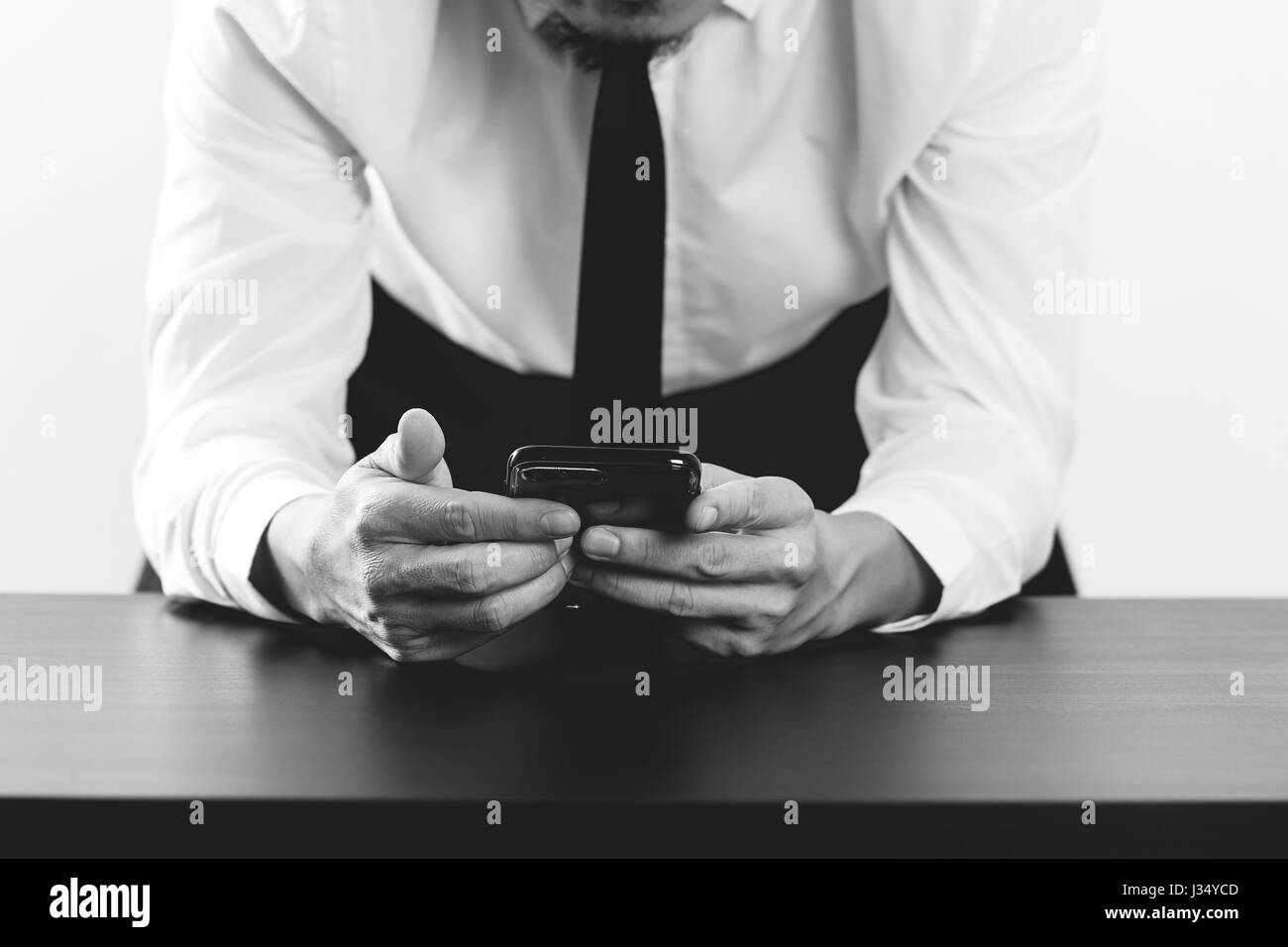 Close up of businessman working with smart phone sur le bureau en bois bureau moderne en noir et blanc, Banque D'Images
