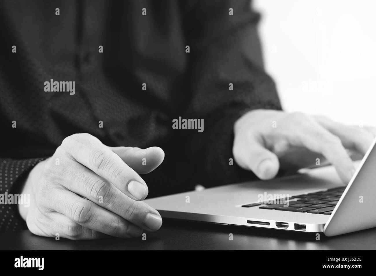 Close up of businessman part travailler avec un ordinateur portable dans un bureau moderne, noir et blanc Banque D'Images