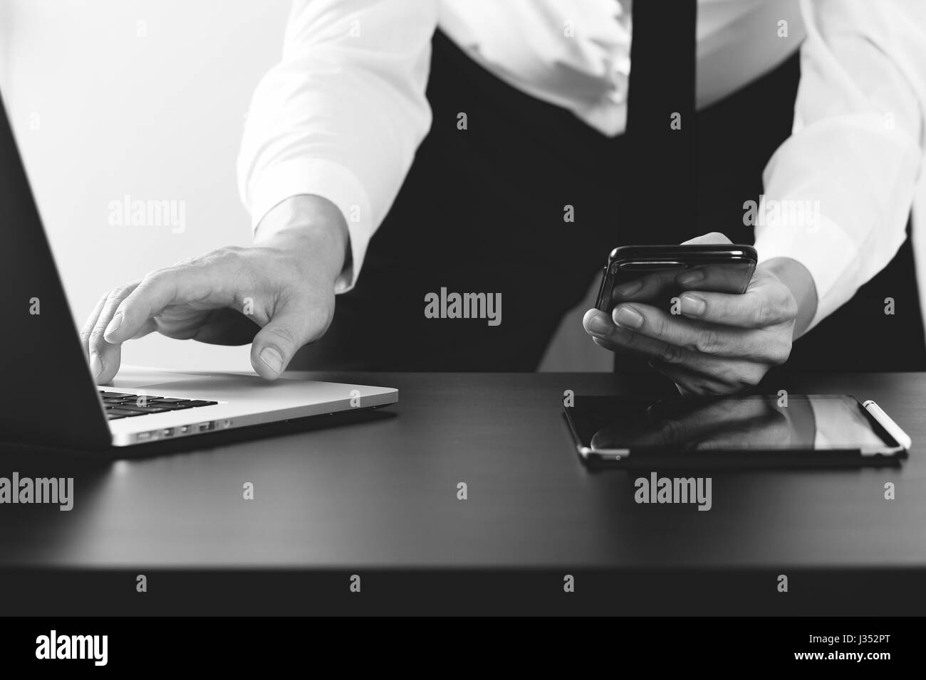 Close up of businessman working with smart phone et l'ordinateur portable et tablette numérique dans l'ordinateur de bureau moderne, noir et blanc Banque D'Images