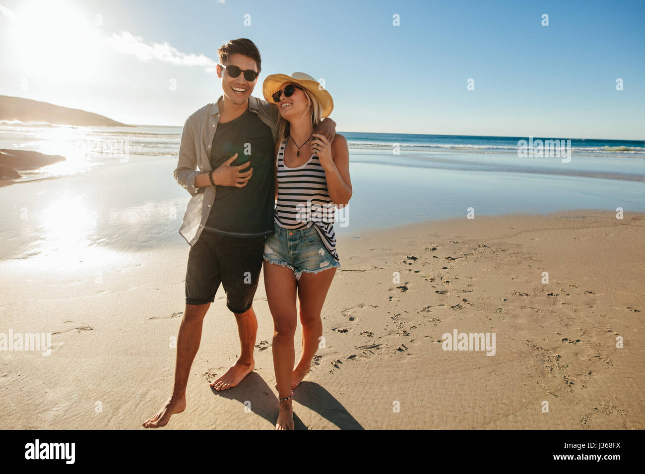 Une photo de couple walking on beach. Jeune homme et femme marche sur le littoral et sourit à une journée d'été. Banque D'Images