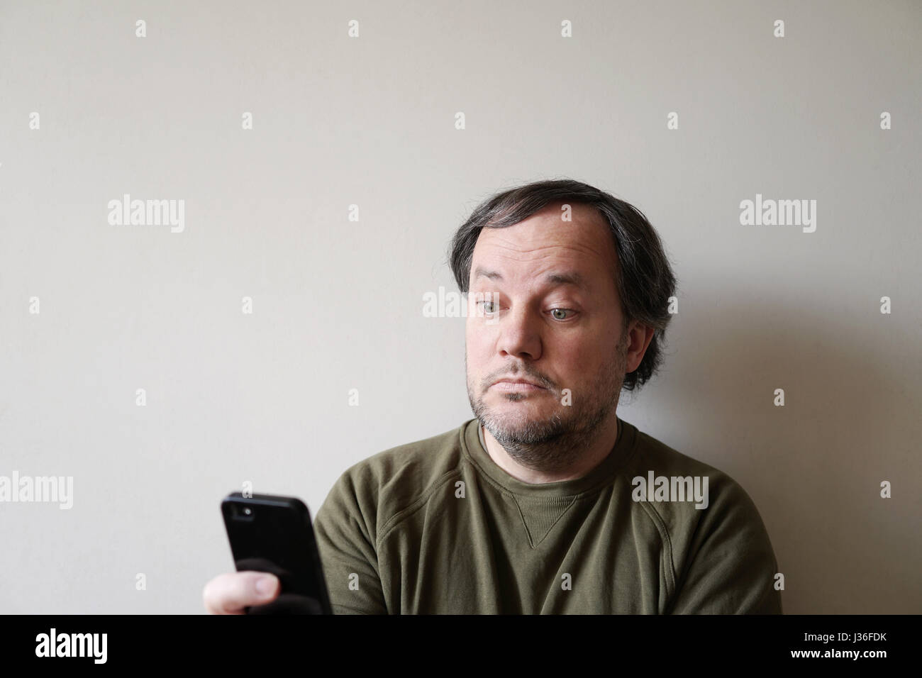 Wide-eyed man looking at smartphone Banque D'Images