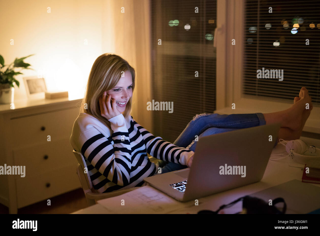 Femme à 24, holding smartphone, travaillant sur l'ordinateur portable dans la nuit. Banque D'Images
