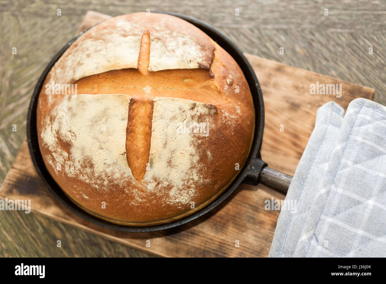 Du pain artisanal de boulangerie nouvellement dans la poêle en fonte sur planche à découper en bois. Manique gris à côté. Banque D'Images