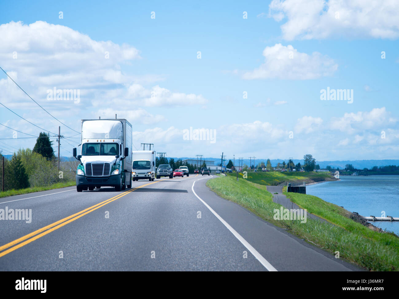 Gros camion blanc semi truck avec cabine de jour et top pour le transport du fret commercial régional se déplace le long de la route en ligne droite le long de la rivière Banque D'Images