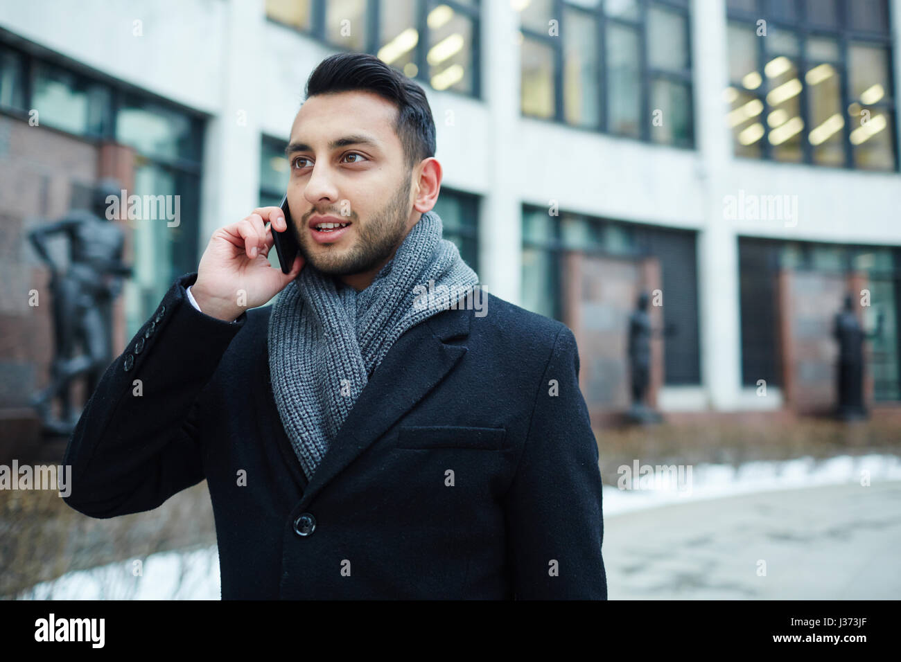 Bel homme du Moyen-Orient s'exprimant par téléphone en ville Banque D'Images