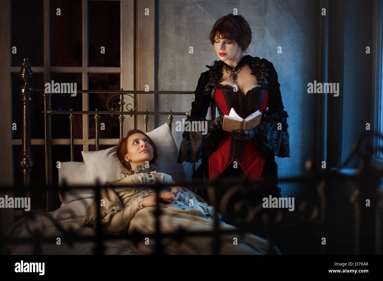 Femme malade allongé sur un lit à côté d'une autre femme lisant un livre, dans le style gothique rétro. Banque D'Images