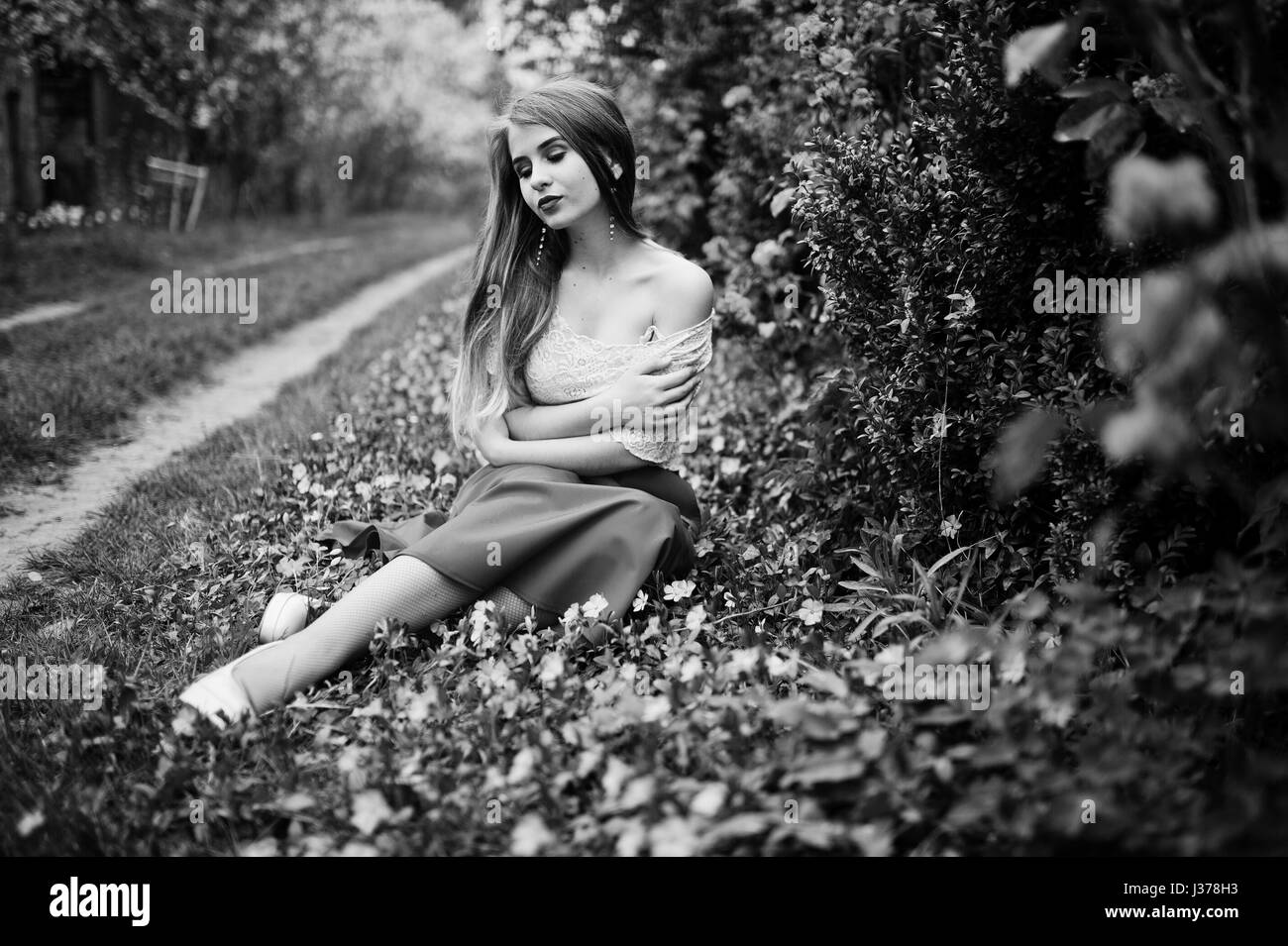 Portrait de sitiing belle fille avec lèvres rouge à fleur de printemps sur l'herbe du jardin de fleurs, l'usure de robe rouge et chemise blanche. Banque D'Images